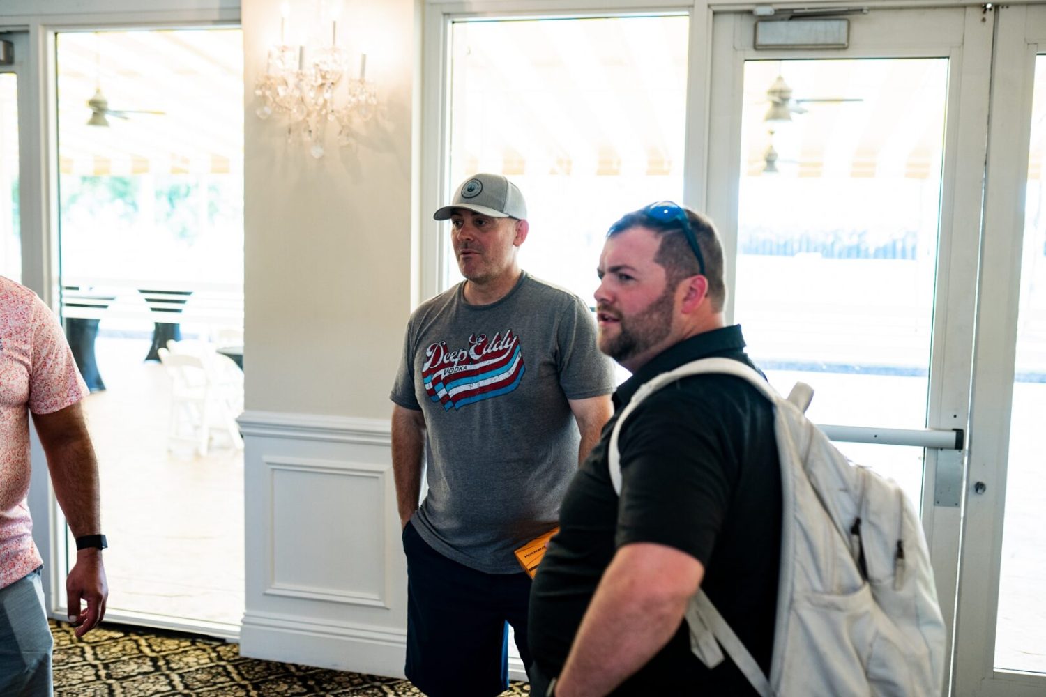 Two men standing in a room with backpacks.