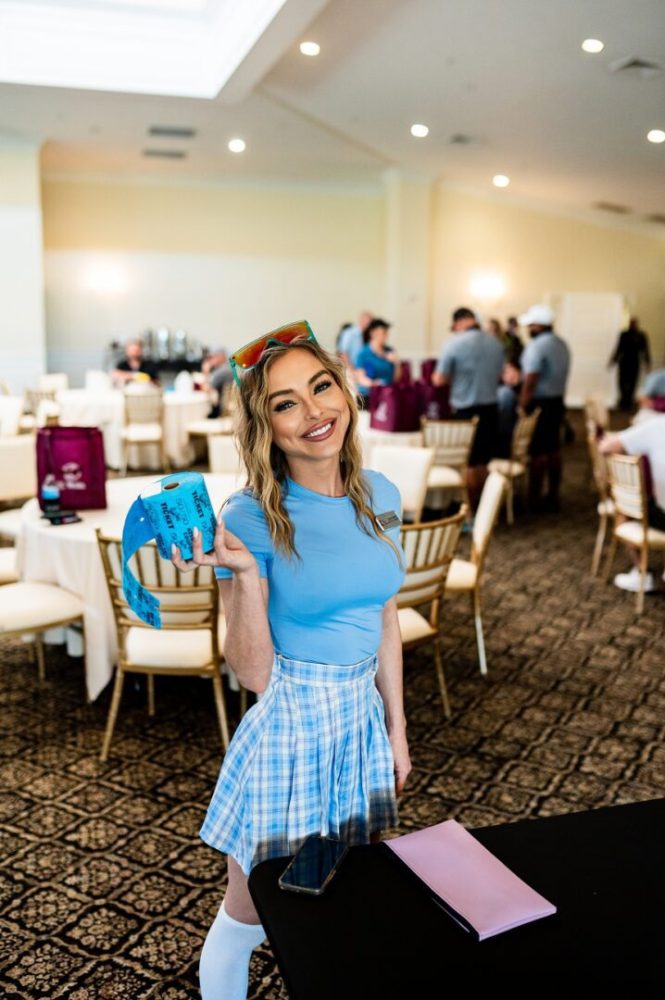 A woman in blue shirt and skirt standing near chairs.