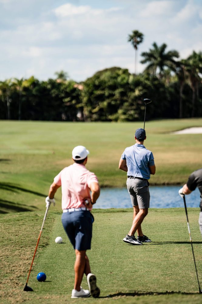 Three men playing golf on a green with trees in the background.