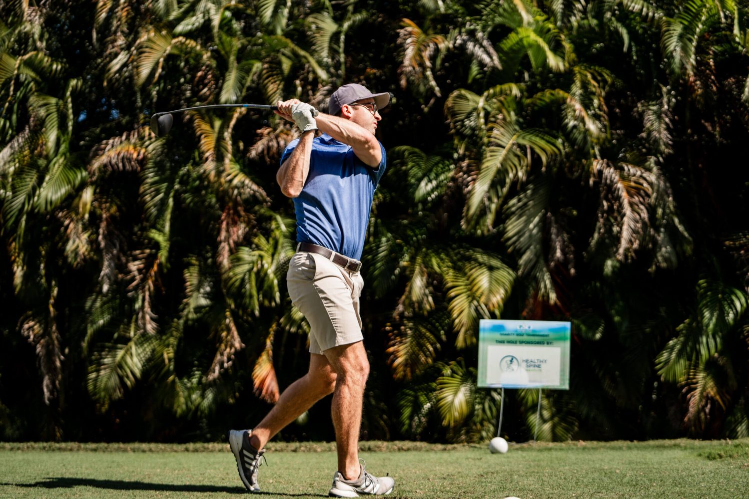 A man swinging at a golf ball on the green.