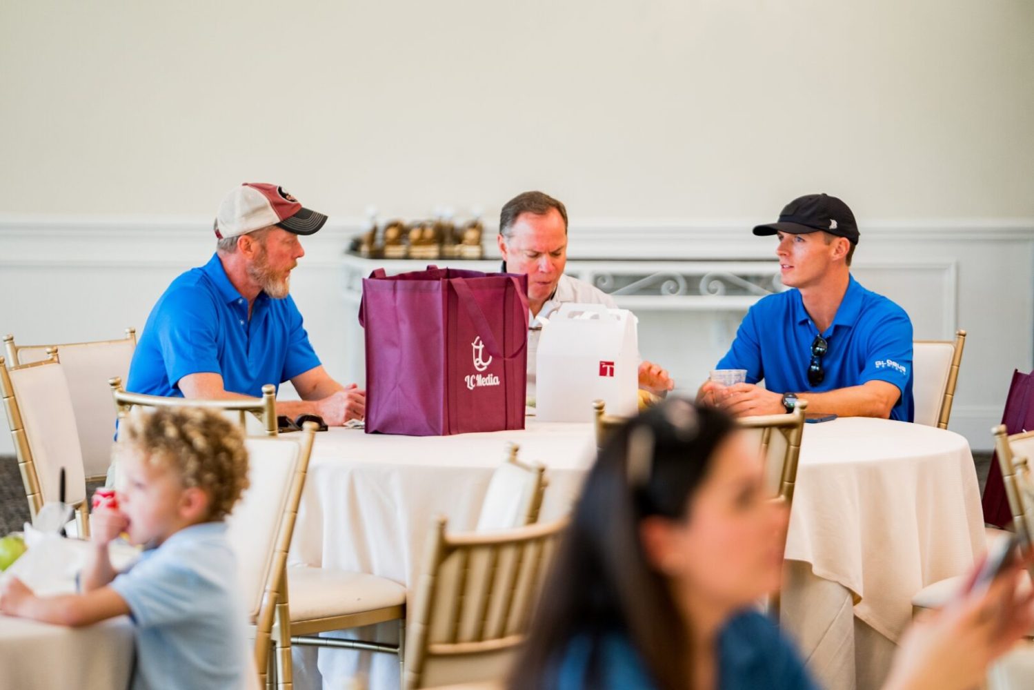 Three men sitting at a table with a bag of food.