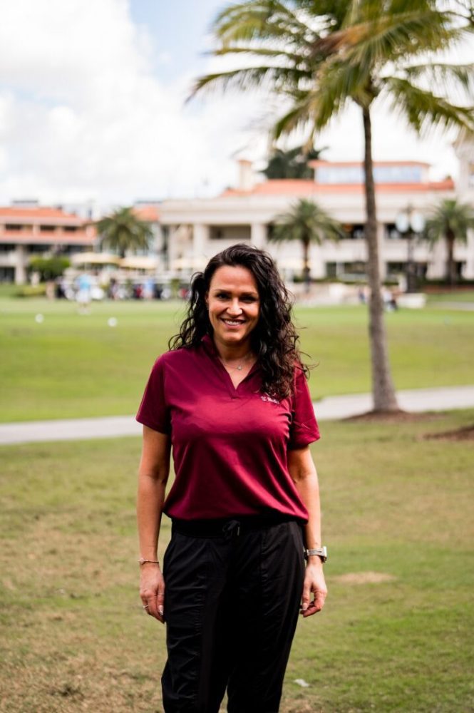 A woman standing in the grass near some trees.