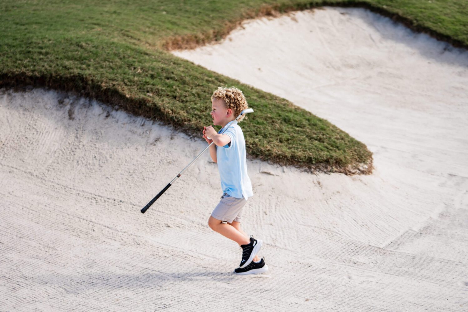 A young boy holding a baseball bat in the sand.