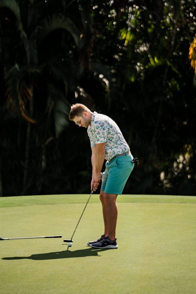 A man in blue shorts and white shirt playing golf.