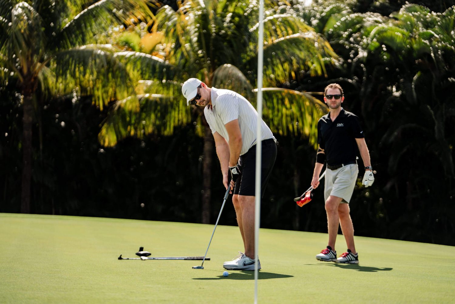 Two men playing golf on a green with palm trees in the background.