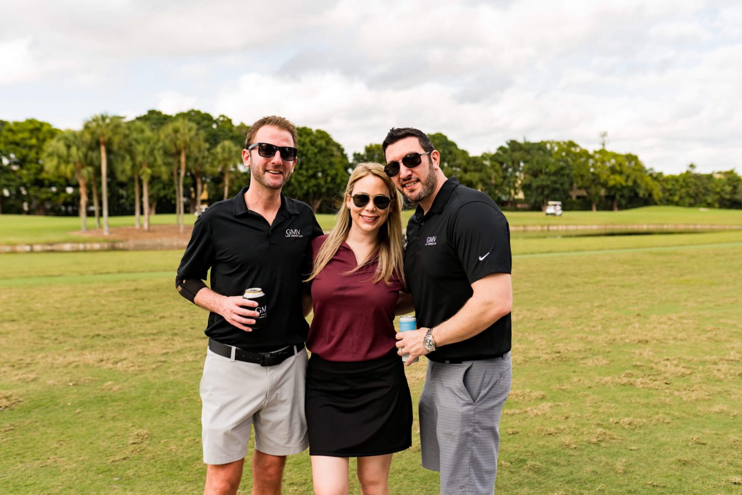 Three people standing in a field holding beers.