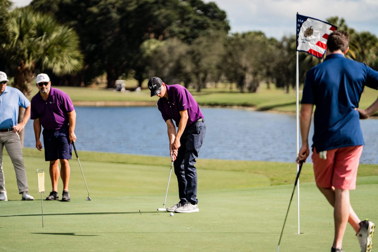 Three people playing golf on a green near water.