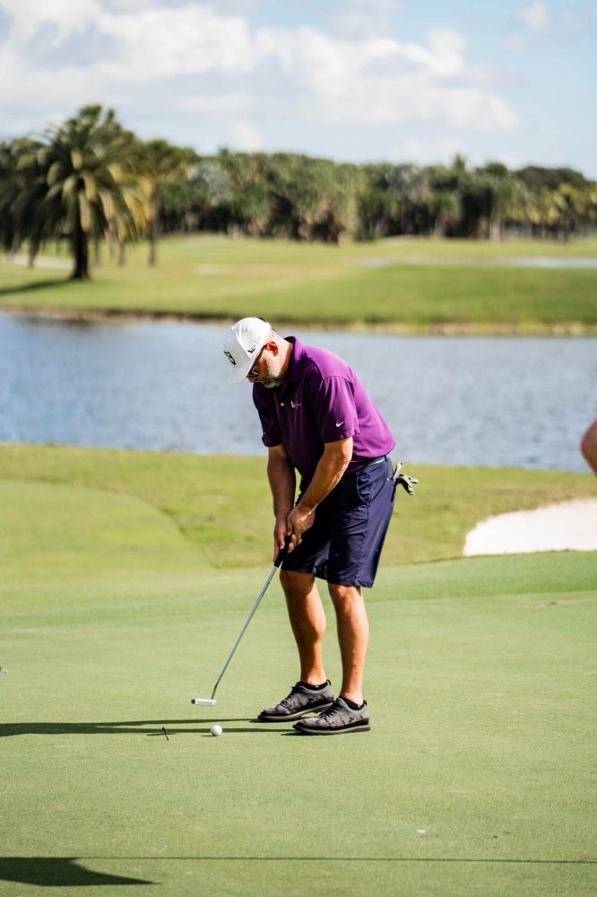 A man in purple shirt playing golf on green.