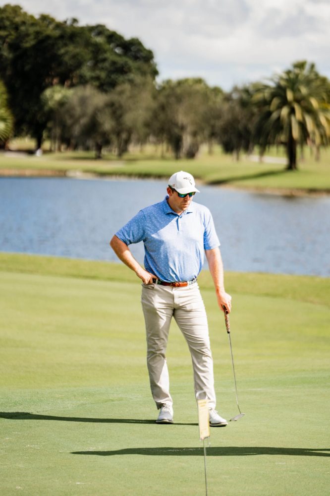 A man standing on top of a golf course holding his hands behind his back.