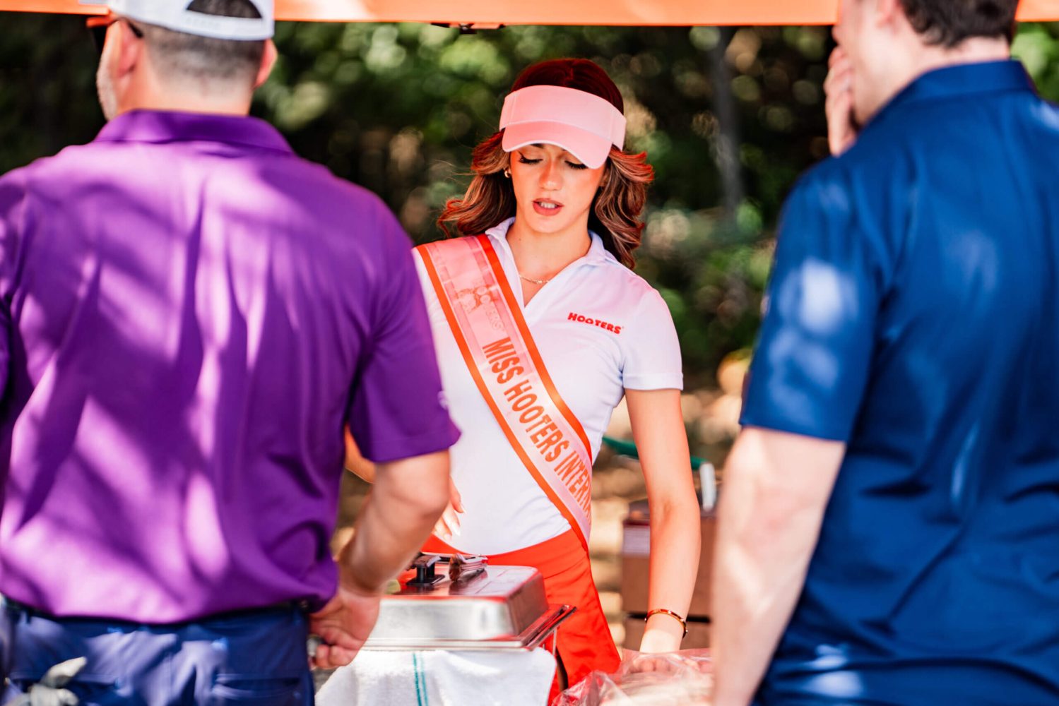 A woman in a pink sash standing next to two men.