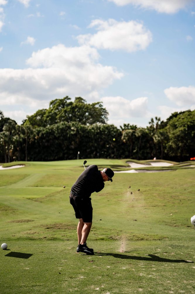 A man playing golf on the green with trees in the background.