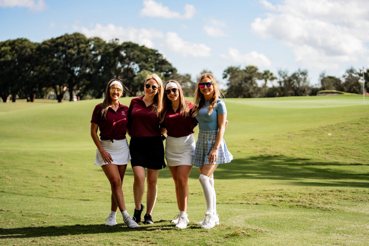 Four women standing on a golf course posing for the camera.