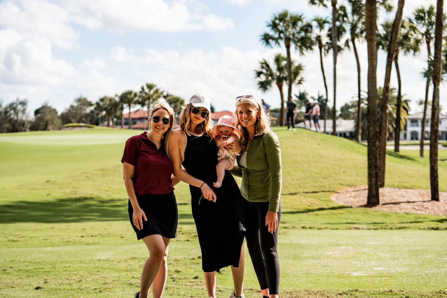 Four women standing in a park with one holding a baby.