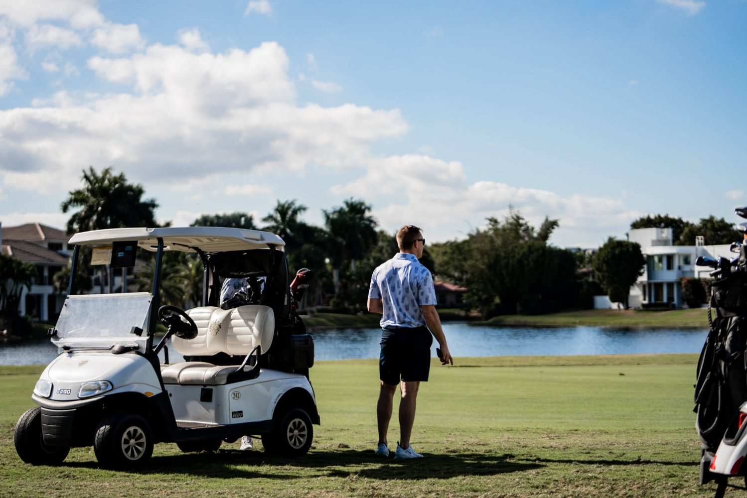 A man standing next to a golf cart on the course.