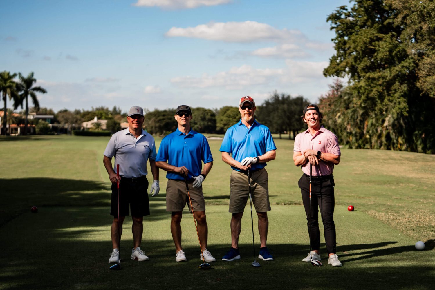Four men standing on a golf course holding their clubs.