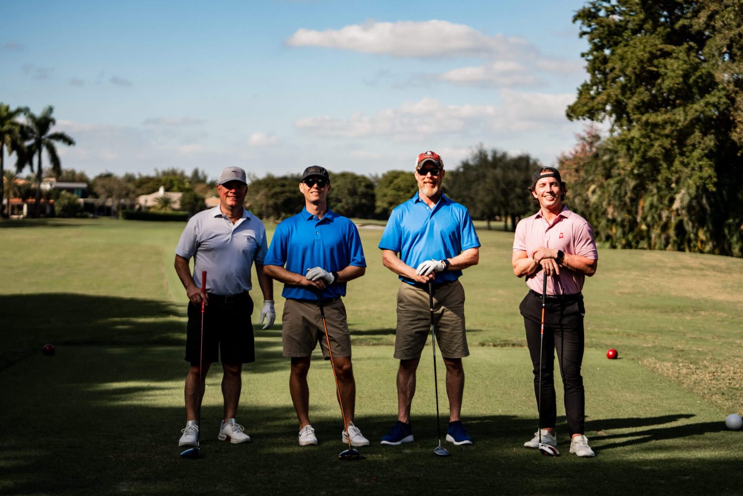 Four men standing on a golf course holding their clubs.