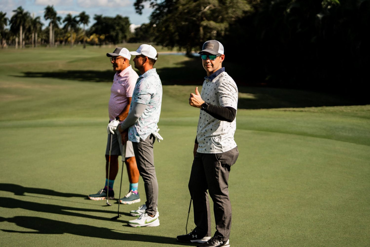 Three men standing on a golf course holding onto their clubs.