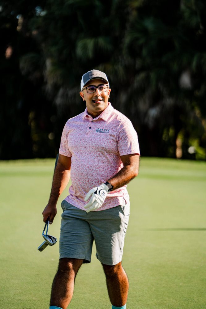 A man in pink shirt holding golf club on green.