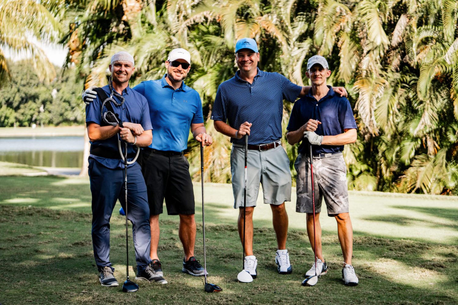Four men standing on a golf course holding their clubs.