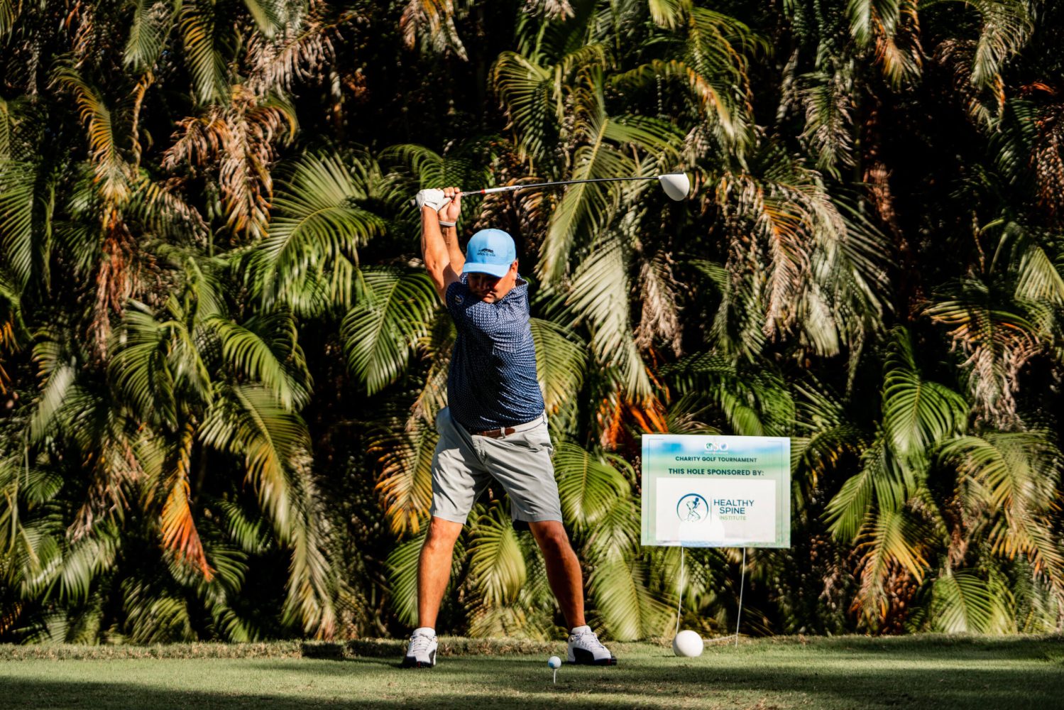 A man swinging at a golf ball on the green.