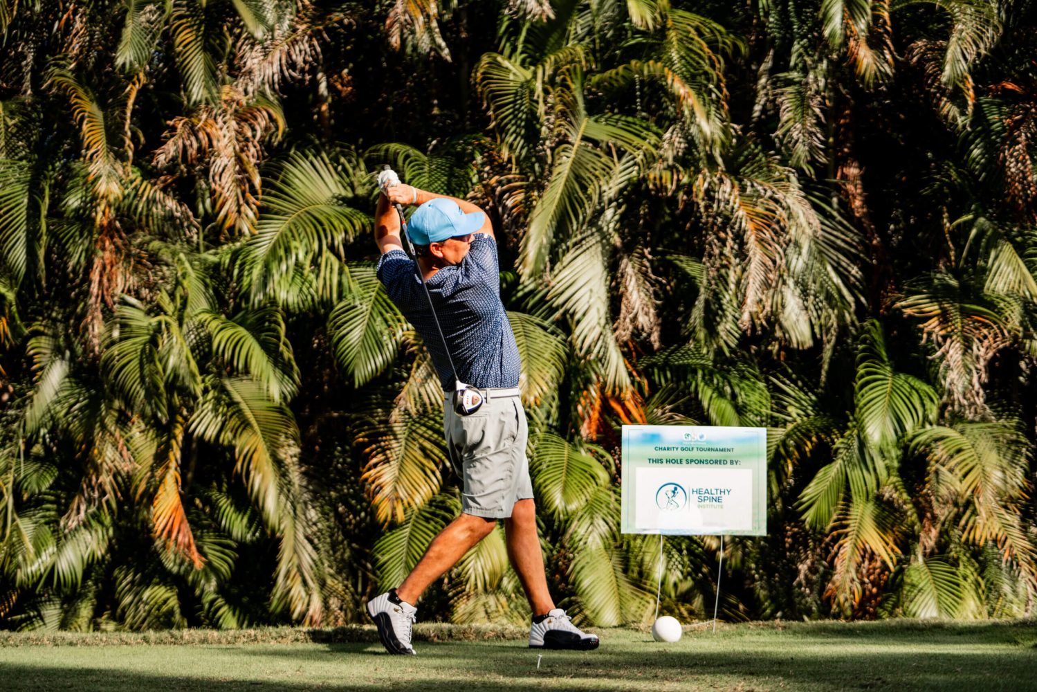 A man swinging at a golf ball on the green.