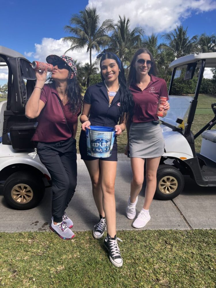 Three women are standing in front of a golf cart.