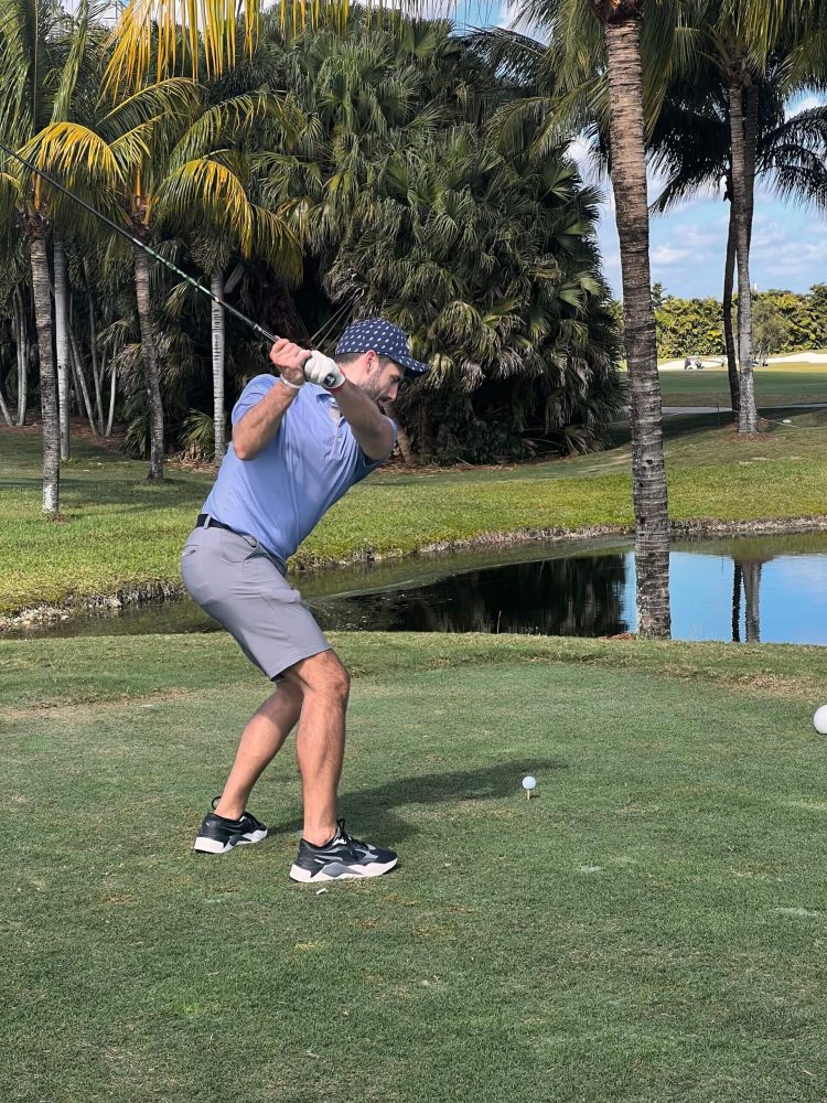 A man swinging at a golf ball on the green.