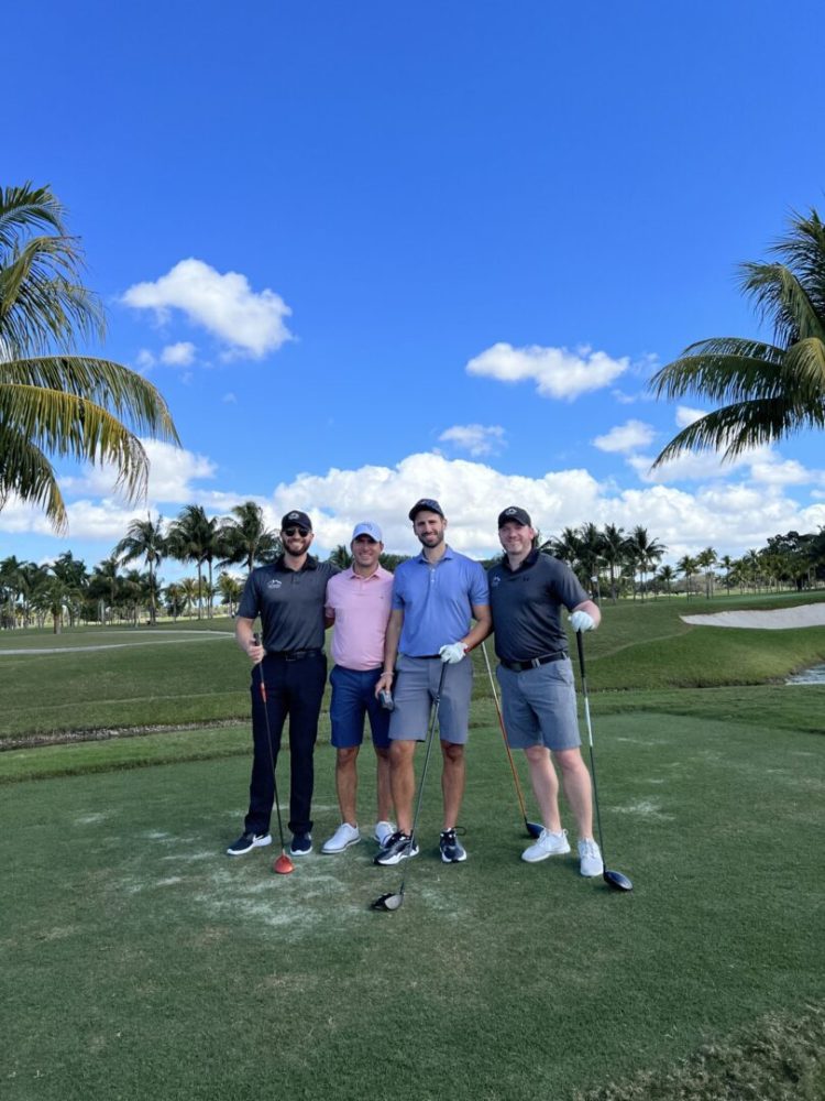 Four people standing on a golf course holding onto their clubs.