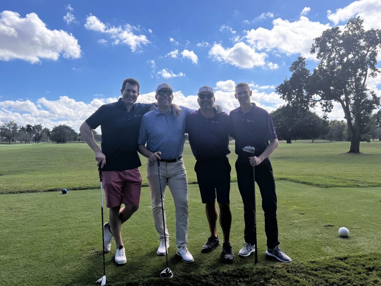 Four men standing on a golf course holding their clubs.