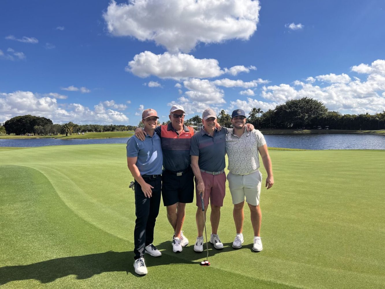 Four men standing on a golf course with their arms around each other.