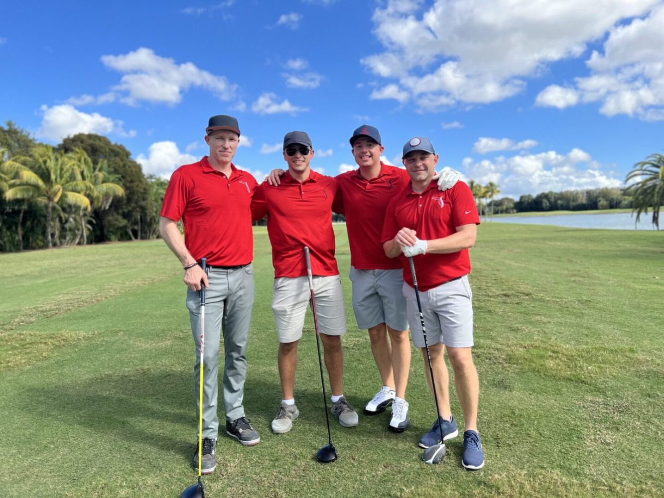 Four men in red shirts and grey shorts standing on a green.