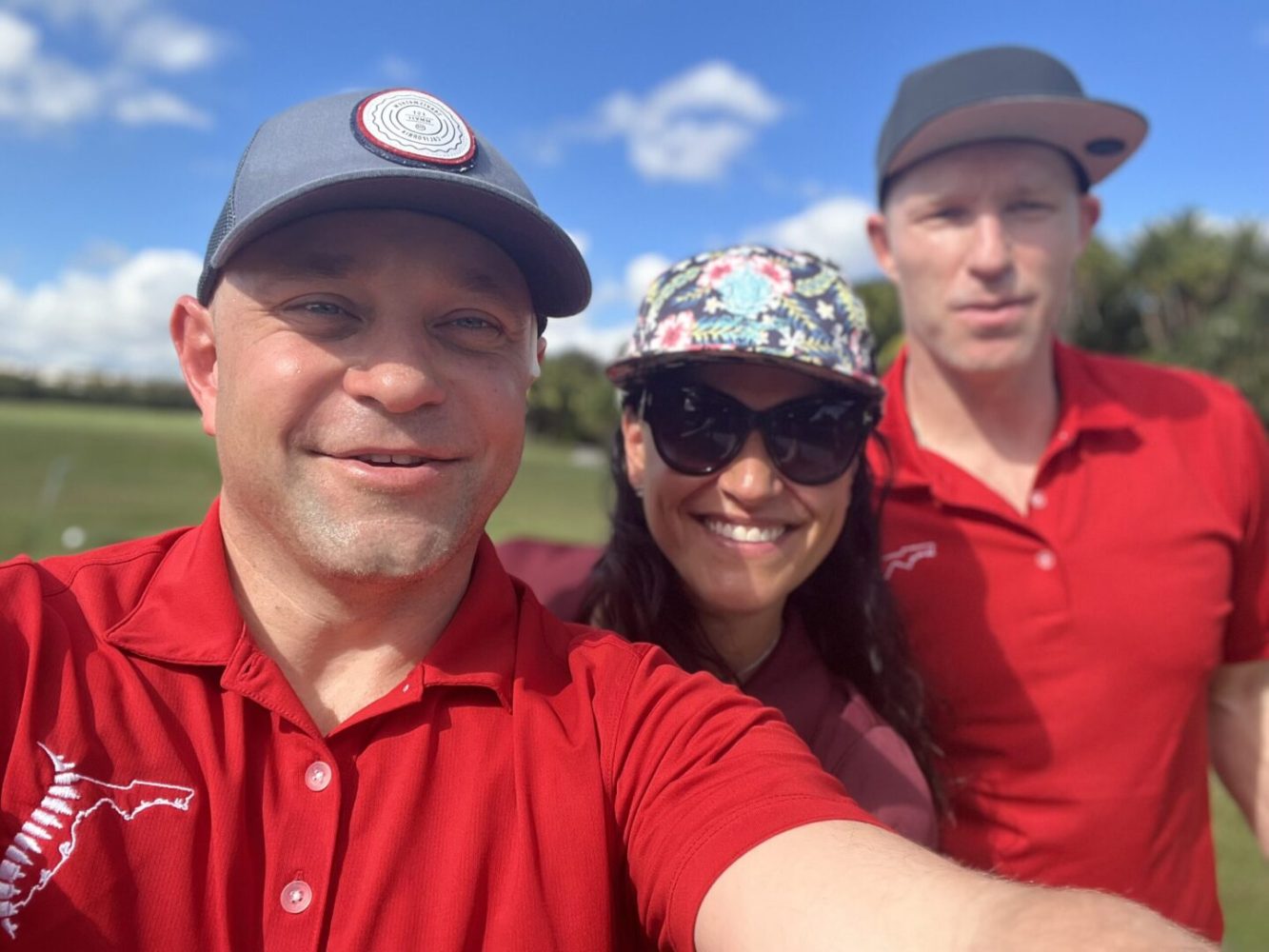 Three people in red shirts and hats taking a selfie.