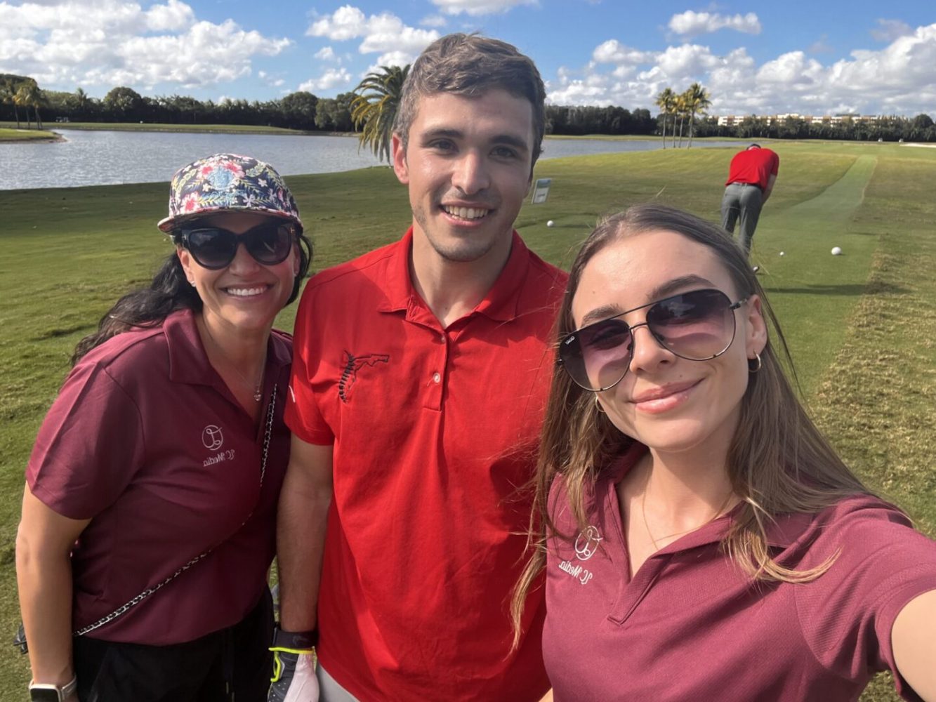 Three people standing on a golf course with water in the background.