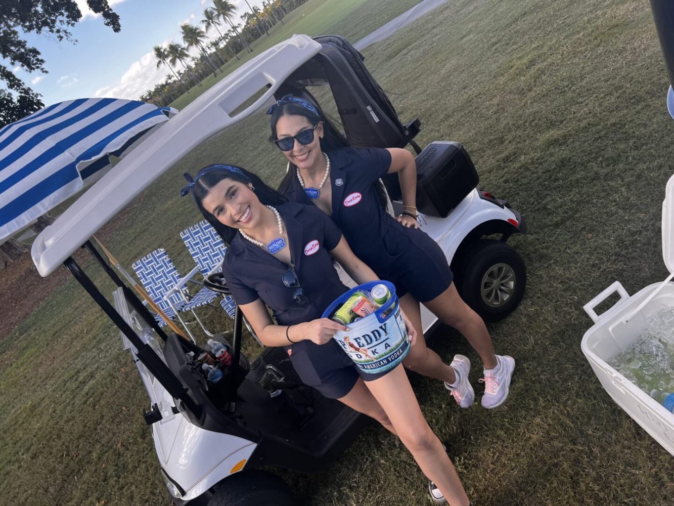 Two women standing in a golf cart holding a bag of ice cream.