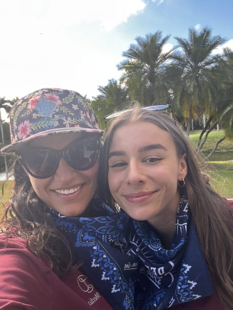 Two women posing for a picture in front of palm trees.