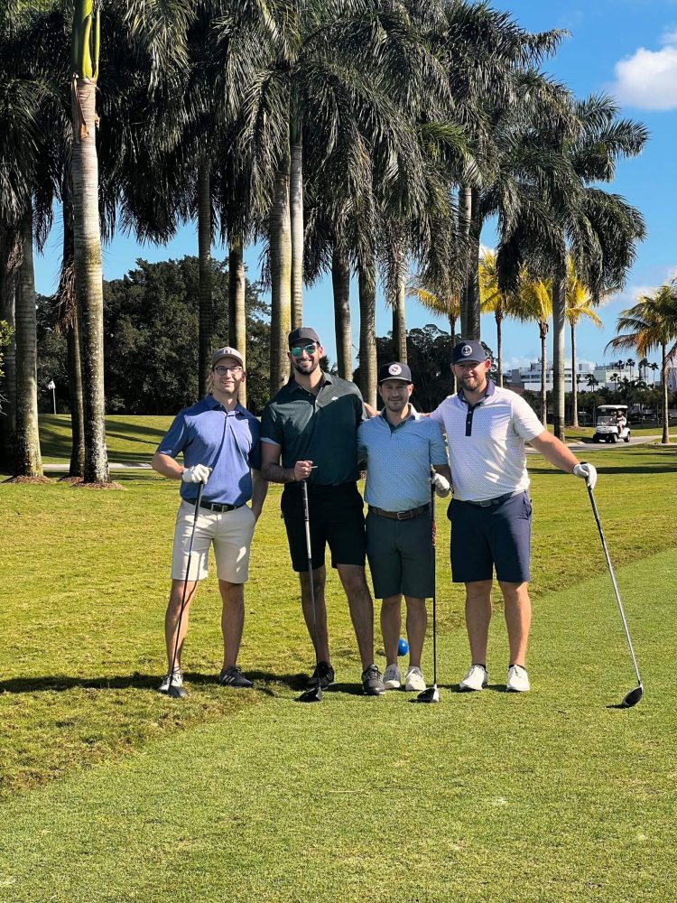Four men standing on a golf course holding onto their clubs.