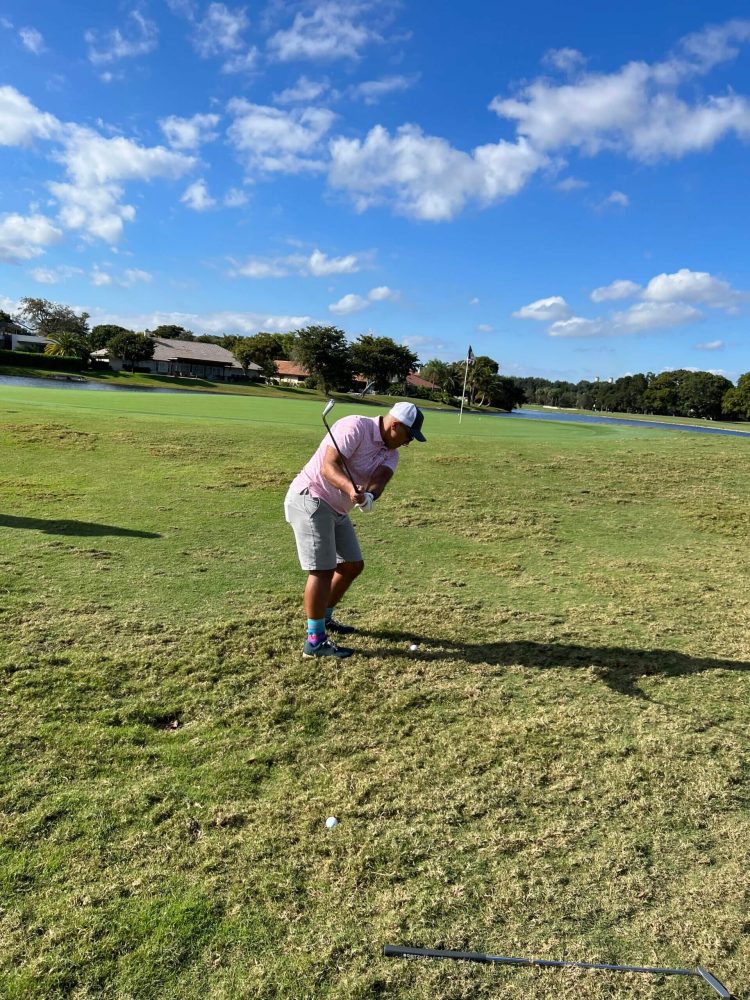 A man in white shirt playing golf on grass.