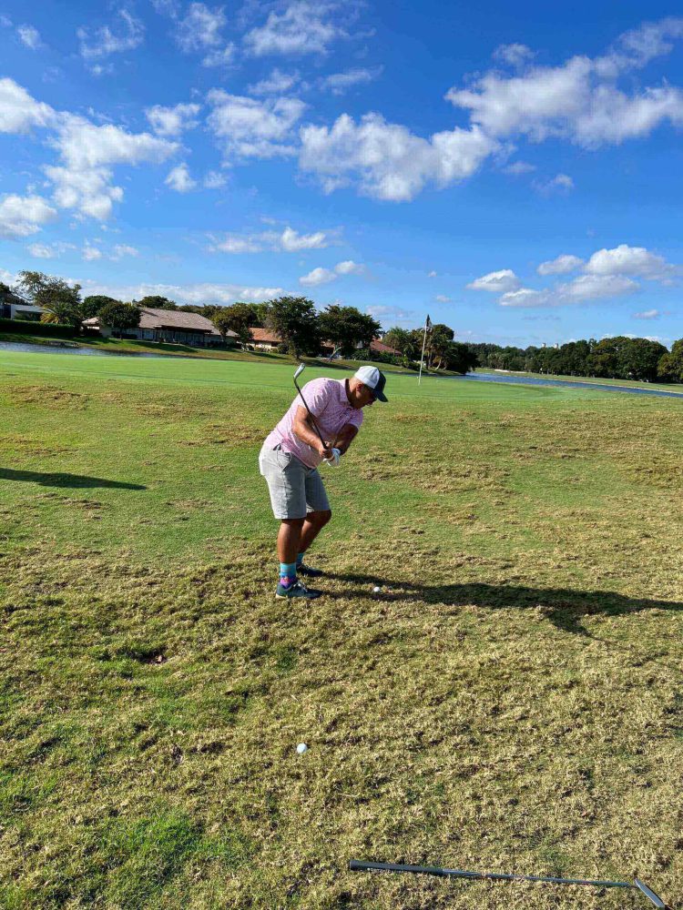 A man in white shirt playing golf on grass.