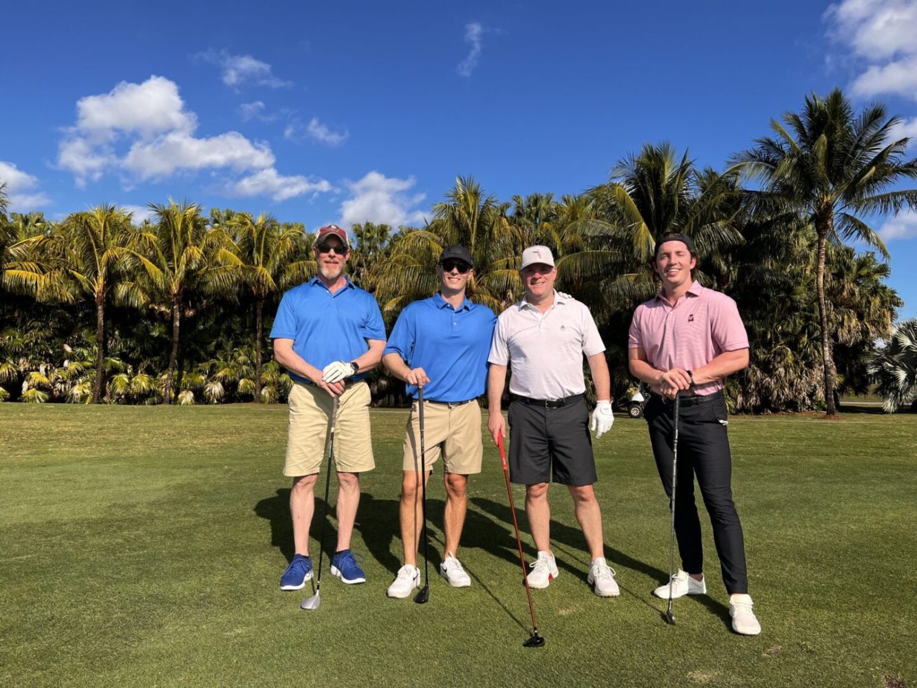 Four men standing on a golf course holding their clubs.