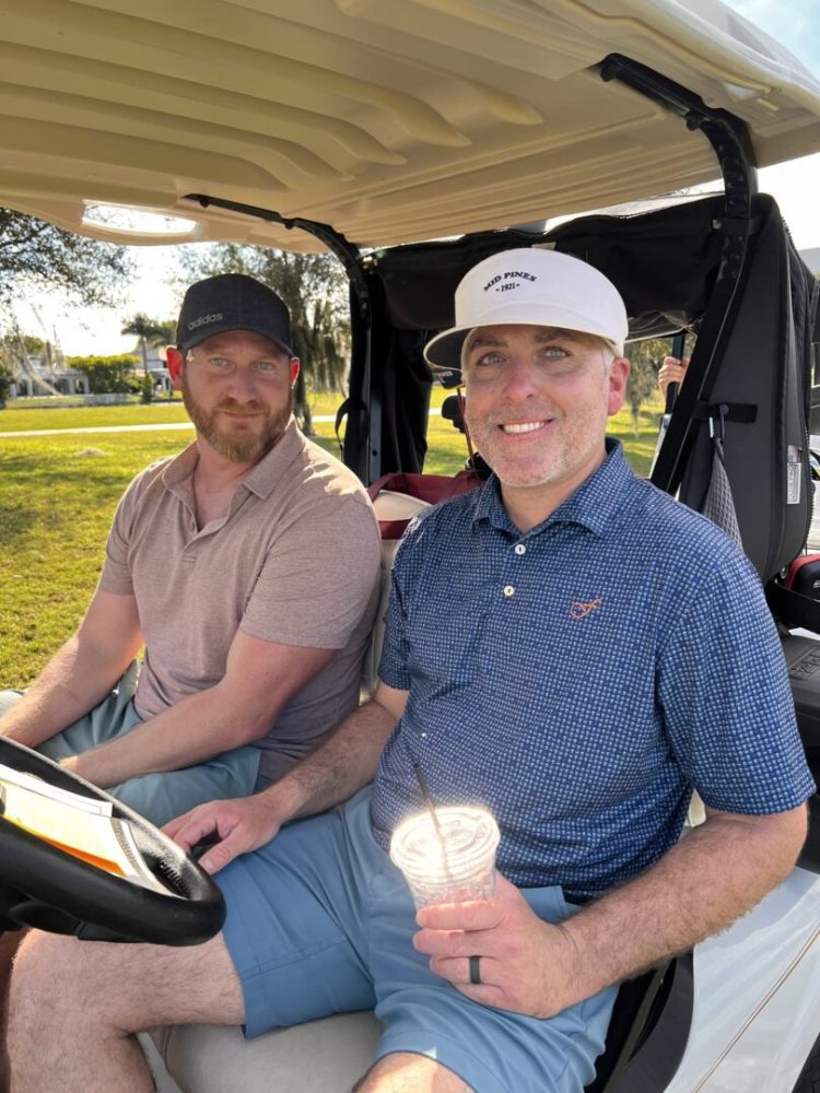 Two men sitting in a golf cart on the course.