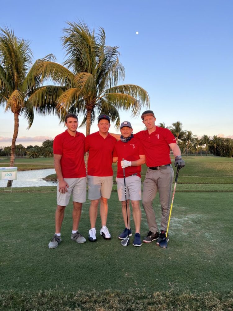 Four men in red shirts are standing on a golf course.